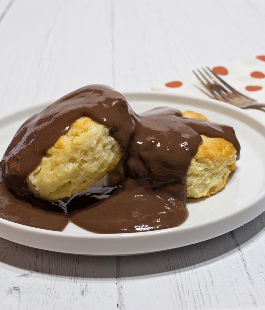 Chocolate gravy poured over biscuits on a white plate.