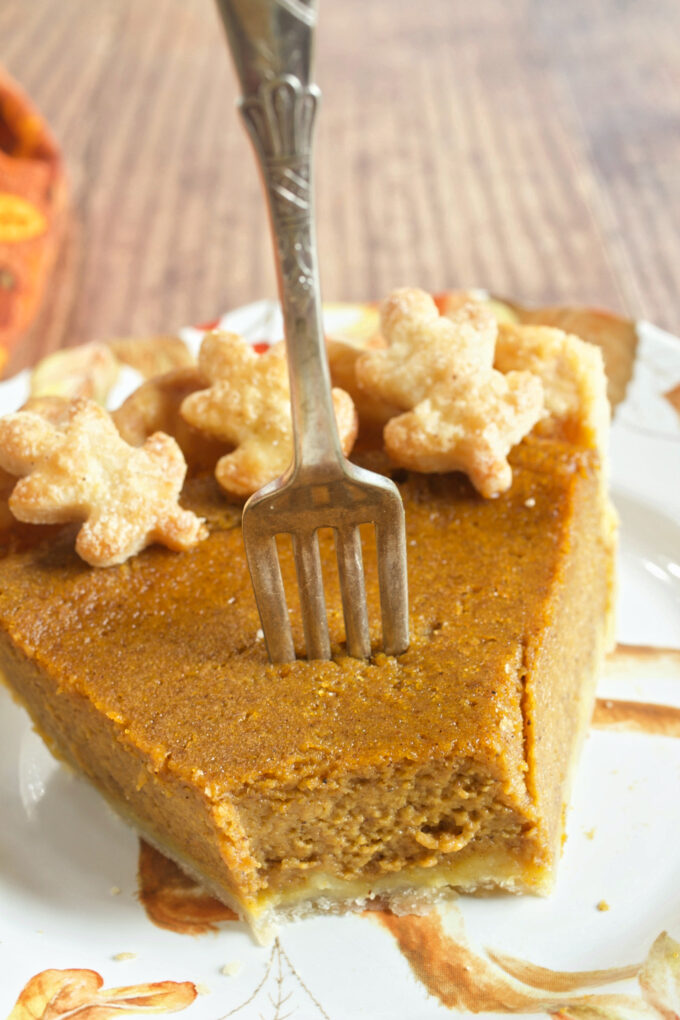 A slice of perfect pumpkin pie with a fork in the top and pastry leaves on the top.