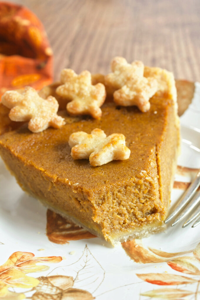 A slice of perfect pumpkin pie with a bite out, a fork beside it, and pastry leaves on top.
