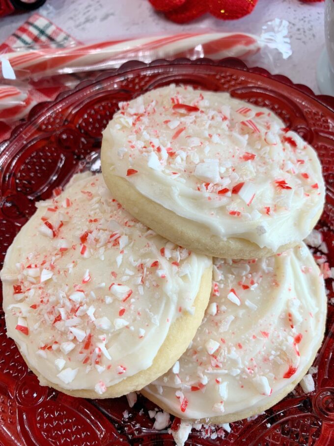 Soft Peppermint Butter Cookies on a red plate with peppermint butter frosting and crushed peppermint candy on top.