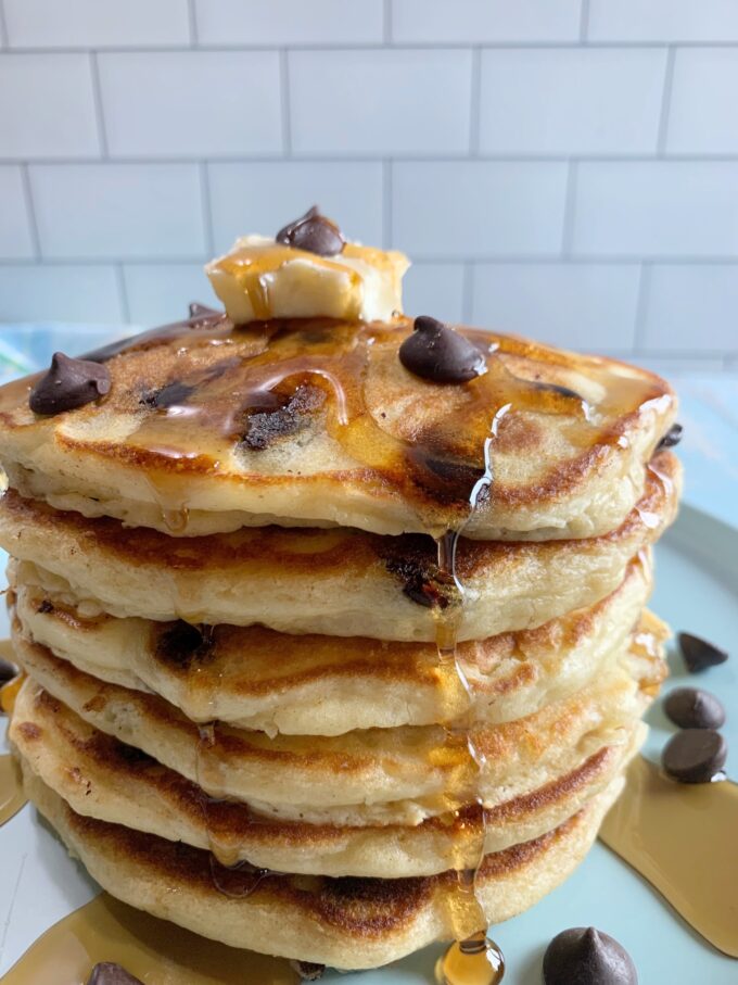 A stack of chocolate chip pancakes with syrup and chocolate chips on a blue plate.