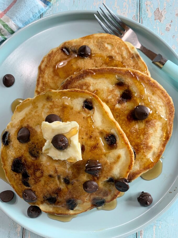 Chocolate Chip Pancakes with chocolate chips and syrup on a blue plate.