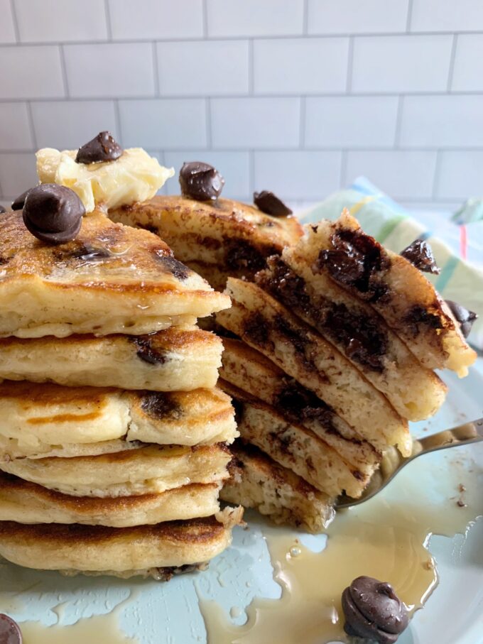 A stack of chocolate chip pancakes with syrup on a blue plate with a forked bite.