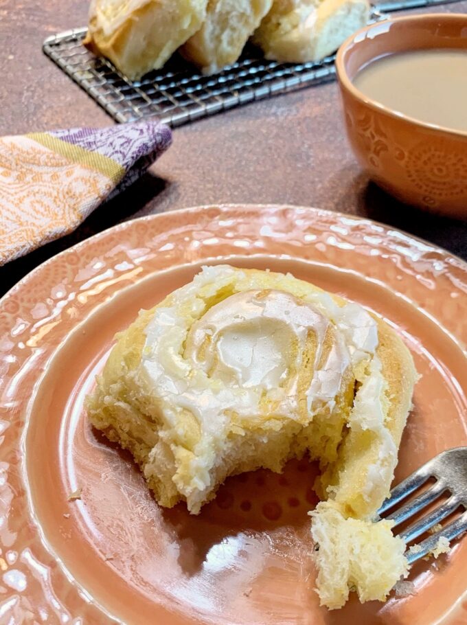 An overnight Orange Roll with a forked bite on an orange dessert plate.