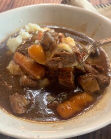 A bowl of beef tips & gravy with carrots over mashed potatoes.