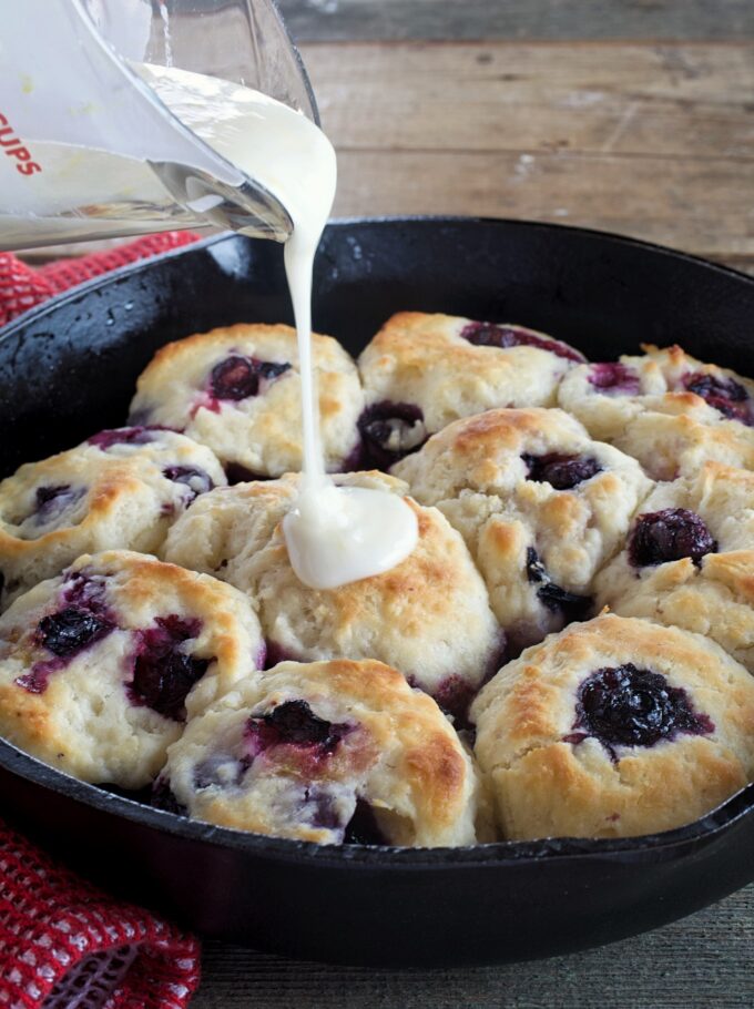 Lemon glaze being poured over blueberry biscuits.