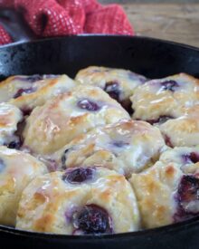 A skillet full of blueberry biscuits with lemon glaze.