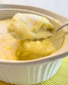 Lemon Cake Custard dessert in a white baking dish with a lifted spoonful.