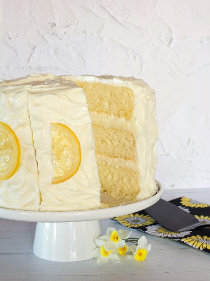A Lemon Layer Cake with a slice out of it on a cake stand.