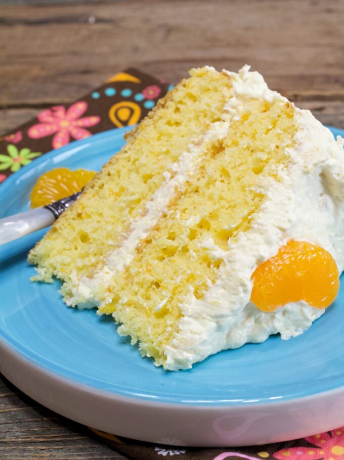 A slice of Mandarin Orange Cake with a forked bite on a blue plate.
