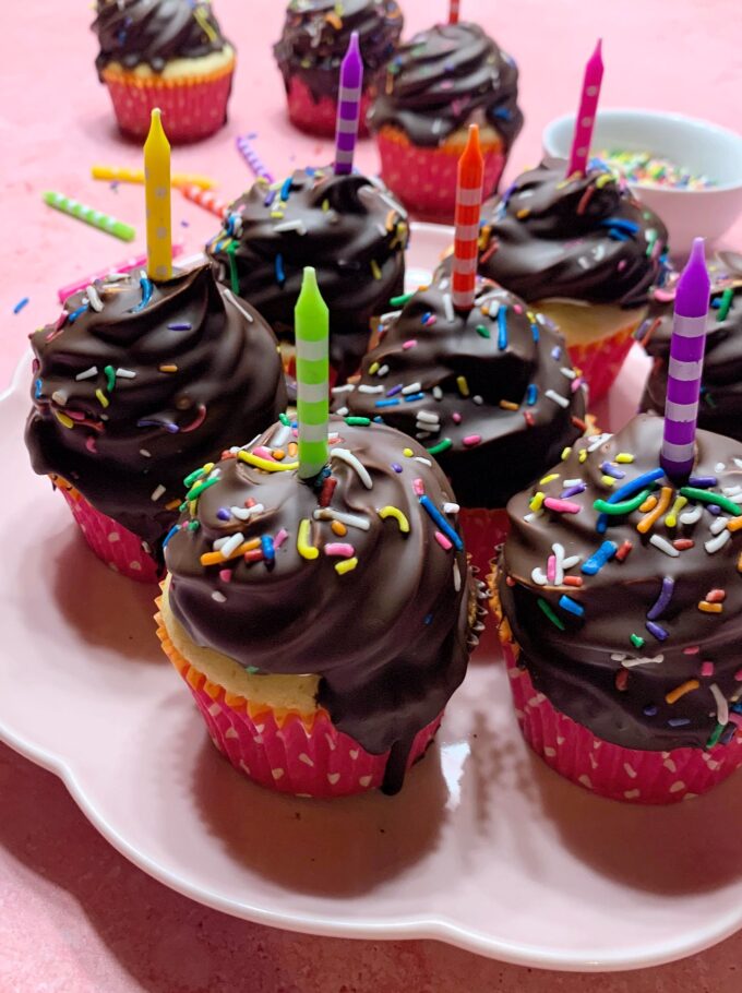 A plate of party cupcakes with chocolate, sprinkles, and candles on top.
