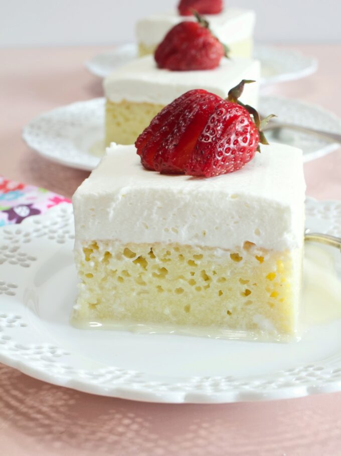 White dessert plates with squares of Tres Leches Cake with strawberries on top.