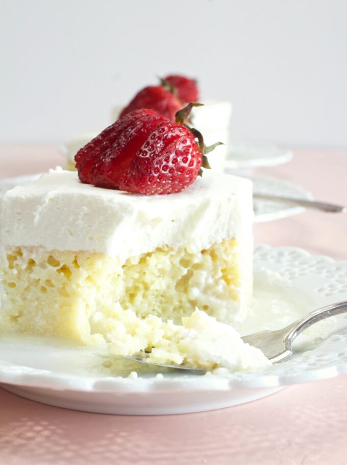 A piece of Tres Leches Cake with strawberries on top and a forked bite.