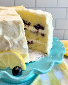 A Lemon Blueberry Cake on a teal cake stand with a slice removed.