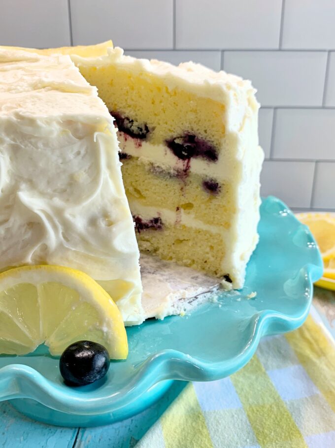 A Lemon Blueberry Cake on a teal cake stand with a slice removed.