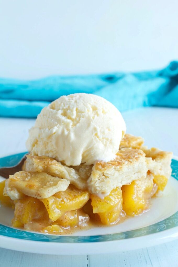 A slice of lattice topped peach pie topped with vanilla ice cream.