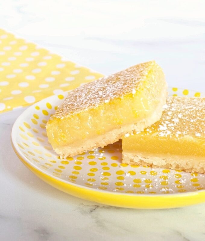 Two lemon bars on a yellow and white plate.