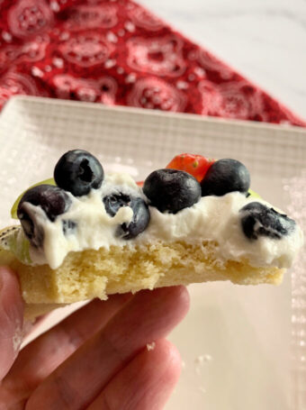 A slice of fruit pizza with a bite out.