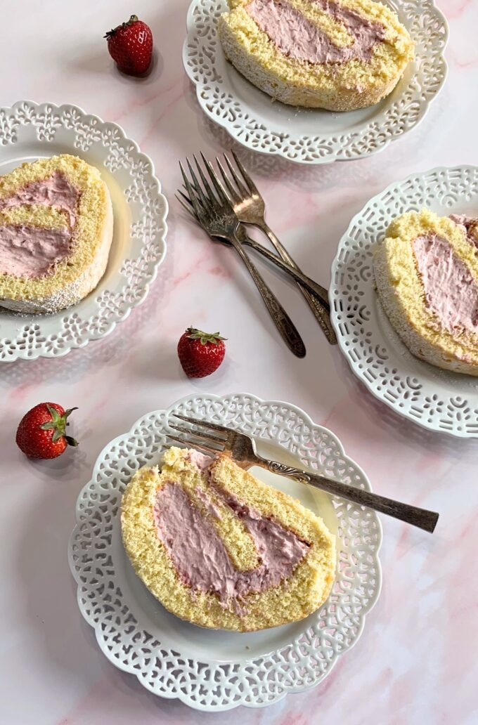Slices of strawberry cream cake roll on plates.